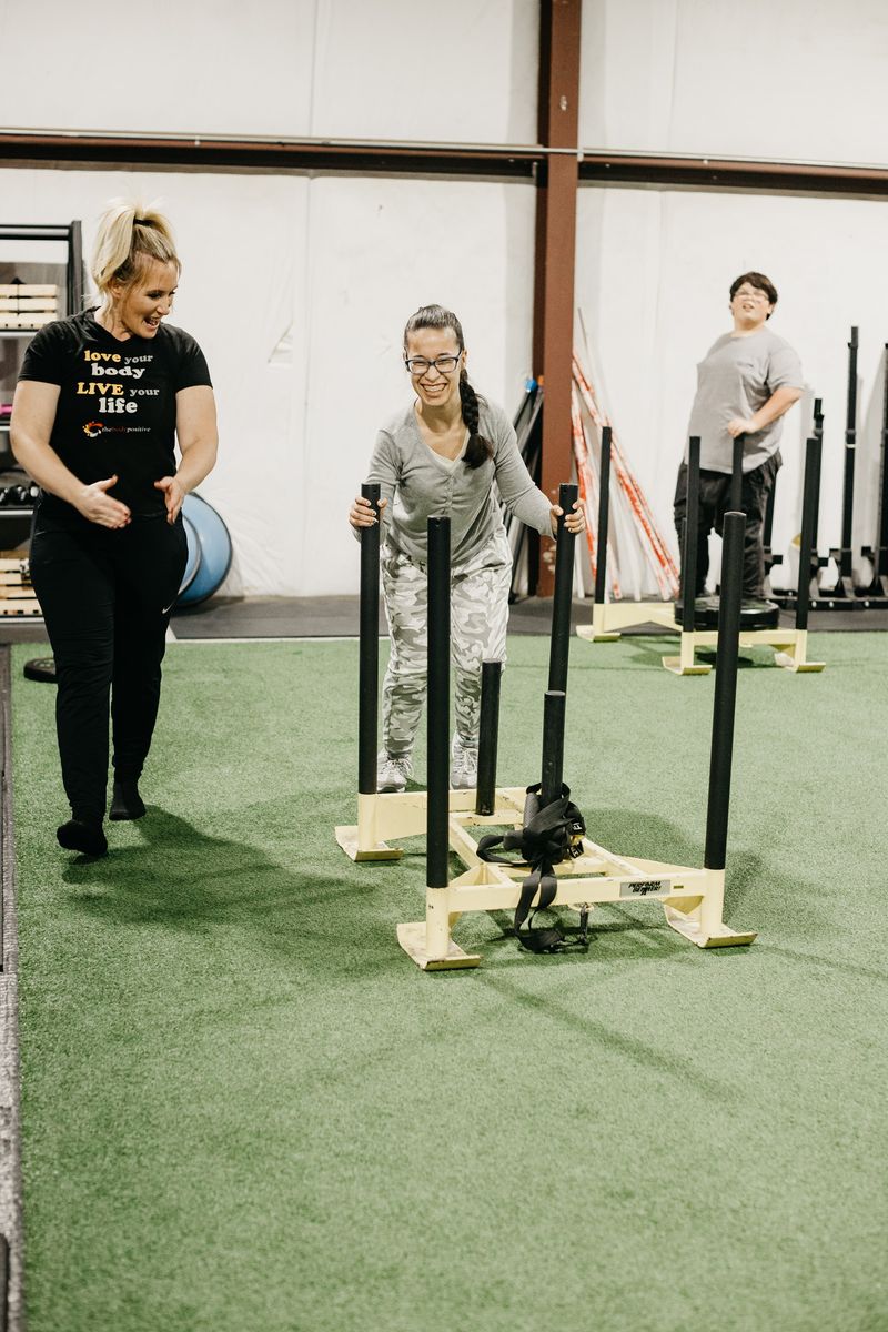 An athlete laughs as she pushes a sled while her coach cheers her on